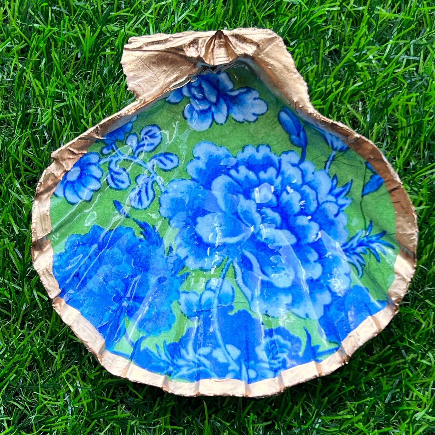A bright green decorative tray with blue roses and gold leaf trim, displayed on a grass-like surface.