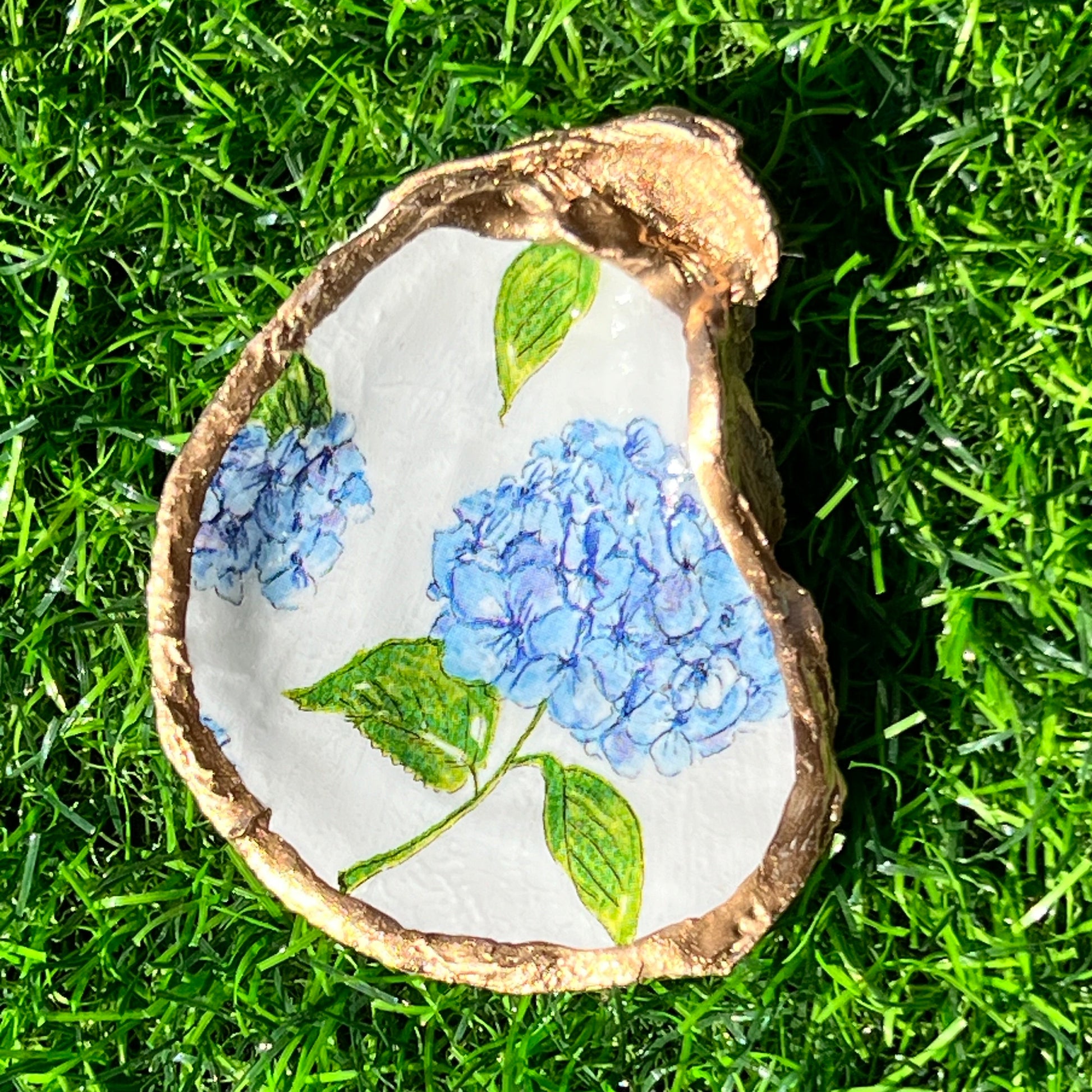 A decorative tray featuring a hydrangea flower design with blue and green colors on a white background, sealed in non-PVC resin with gold leaf trim.