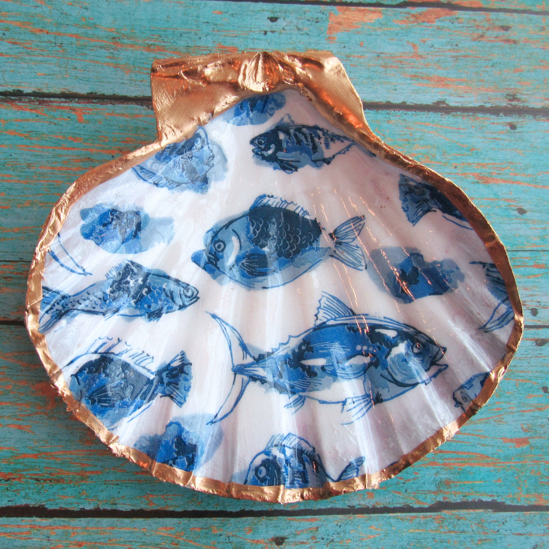 Decorative shell with blue fish pattern on a wooden surface