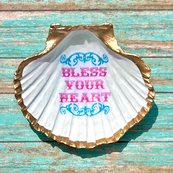 Decorative shell with 'Bless Your Heart' text on a wooden surface